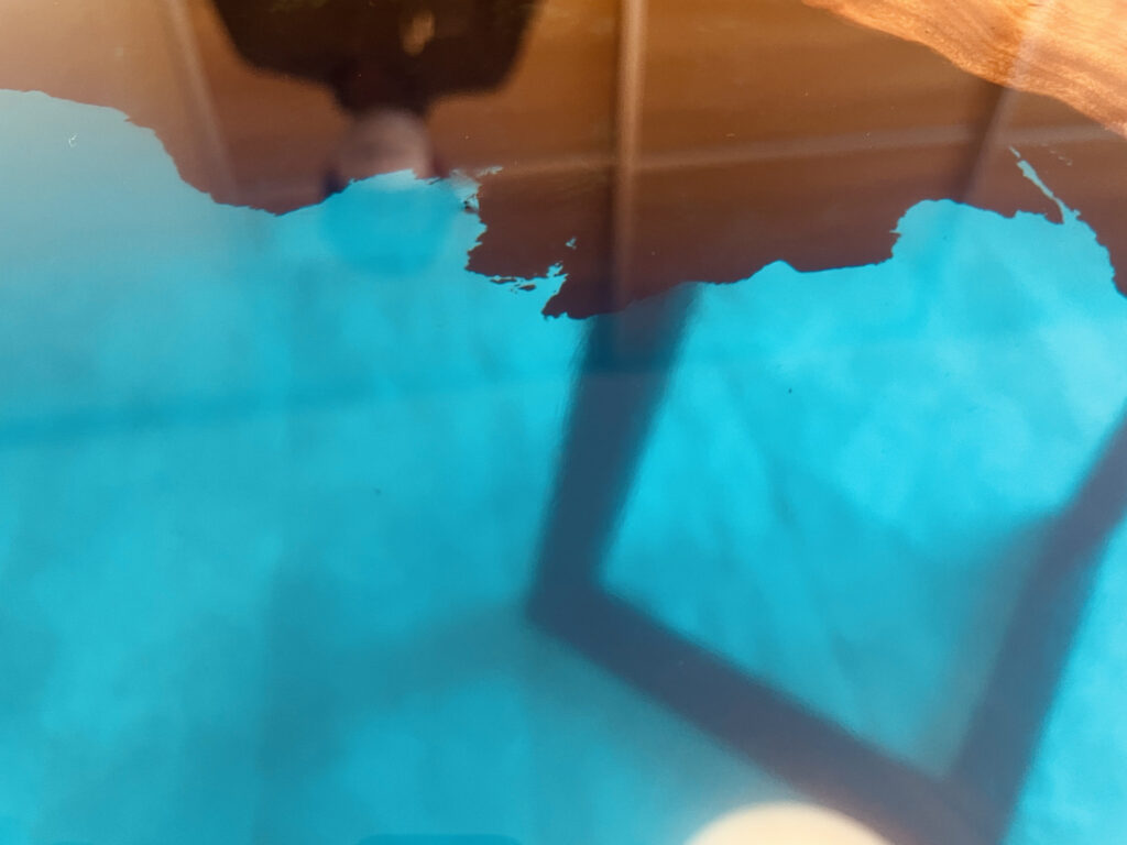 ブルーレジンに家具の脚が映り込むほど、鏡面に仕上げられたレジンテーブルの表面アップ。木の輪郭が鮮明に浮かび上がっている。