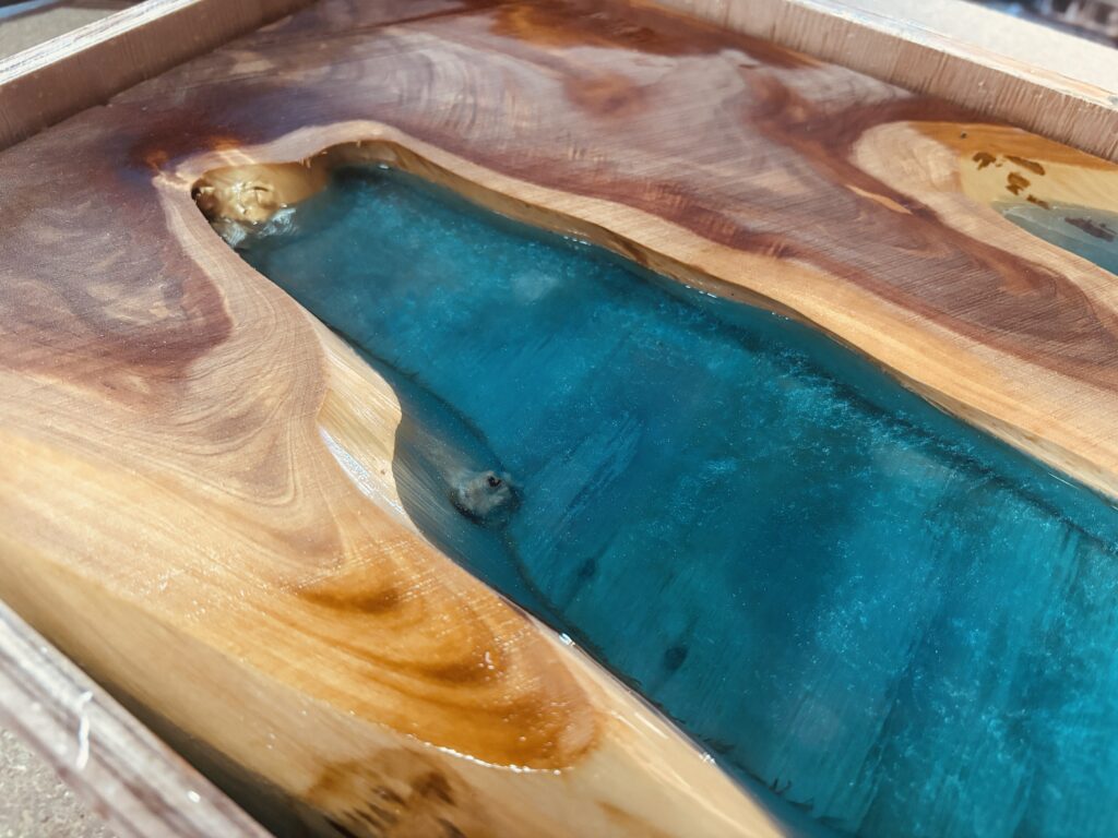カイヅカイブキの複雑な木目に沿って、マイカカラーのグラデーションが入ったブルーグリーンのレジンが美しく硬化している様子。