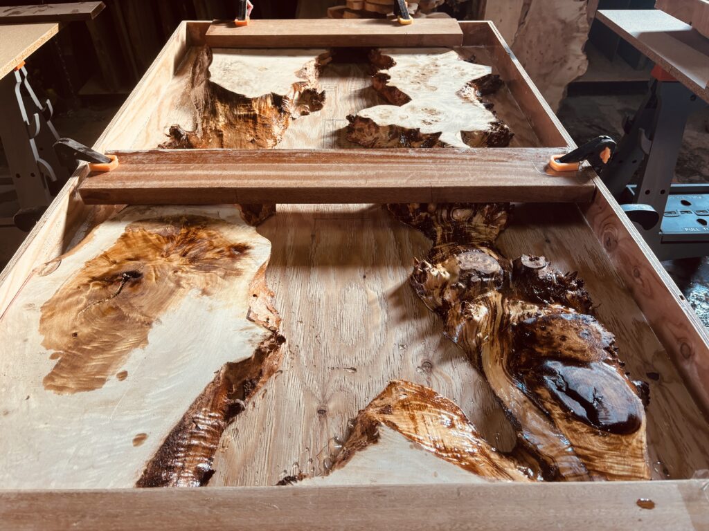 広いアトリエで大型のポプラ材を型枠にセットし、クランプで固定した状態を上から撮影した様子。奥には別の制作中テーブルも見える。