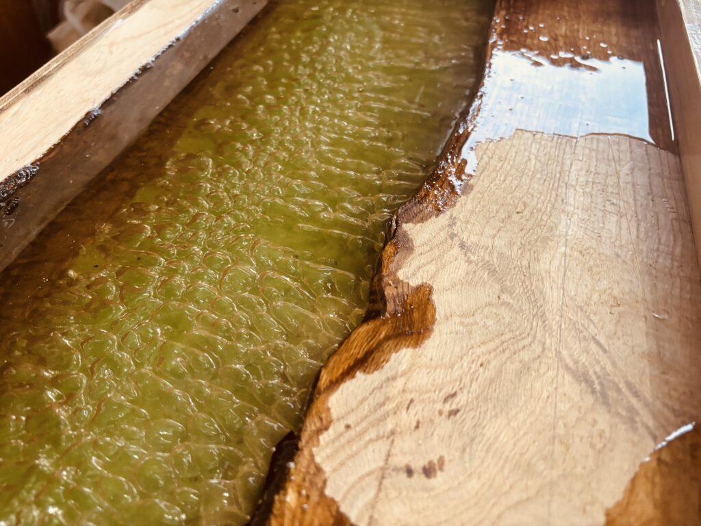 グリーンレジンの泡テクスチャとオーク材の自然な曲線が際立つレジンテーブル制作の接写。