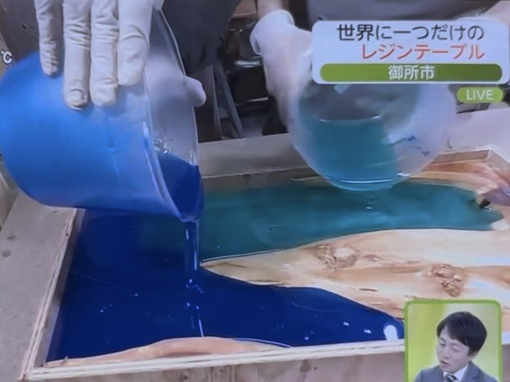 青とエメラルドのレジンを左右から同時に注いでいる映像。無垢材の間を流れ込む様子が映し出されている。