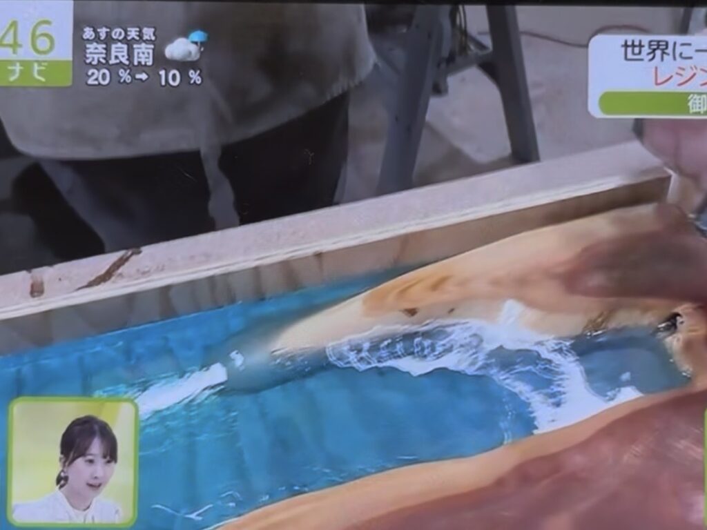 注入されたレジンが波形に広がり、木材の曲線と自然に馴染んでいく様子のクローズアップ映像。