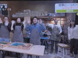 工房で制作体験の関係者全員がカメラに向かって手を振っている生放送のエンディングシーン。