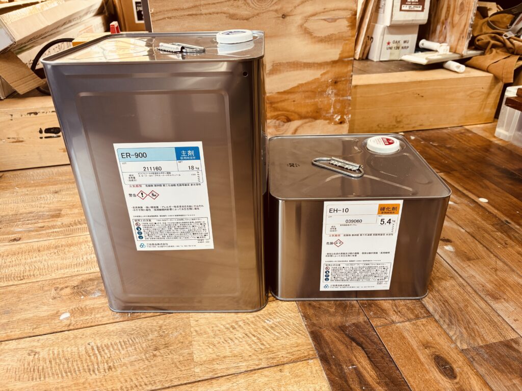 レジンテーブル制作に使用する業務用エポキシ樹脂「ER-900（主剤）」と「EH-10（硬化剤）」の大型金属缶が木の作業台に並んでいる。