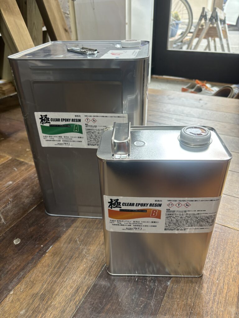 大型缶に入った業務用エポキシレジンA液とB液。レジンテーブル制作に使う主剤と硬化剤が床に並んでいる。