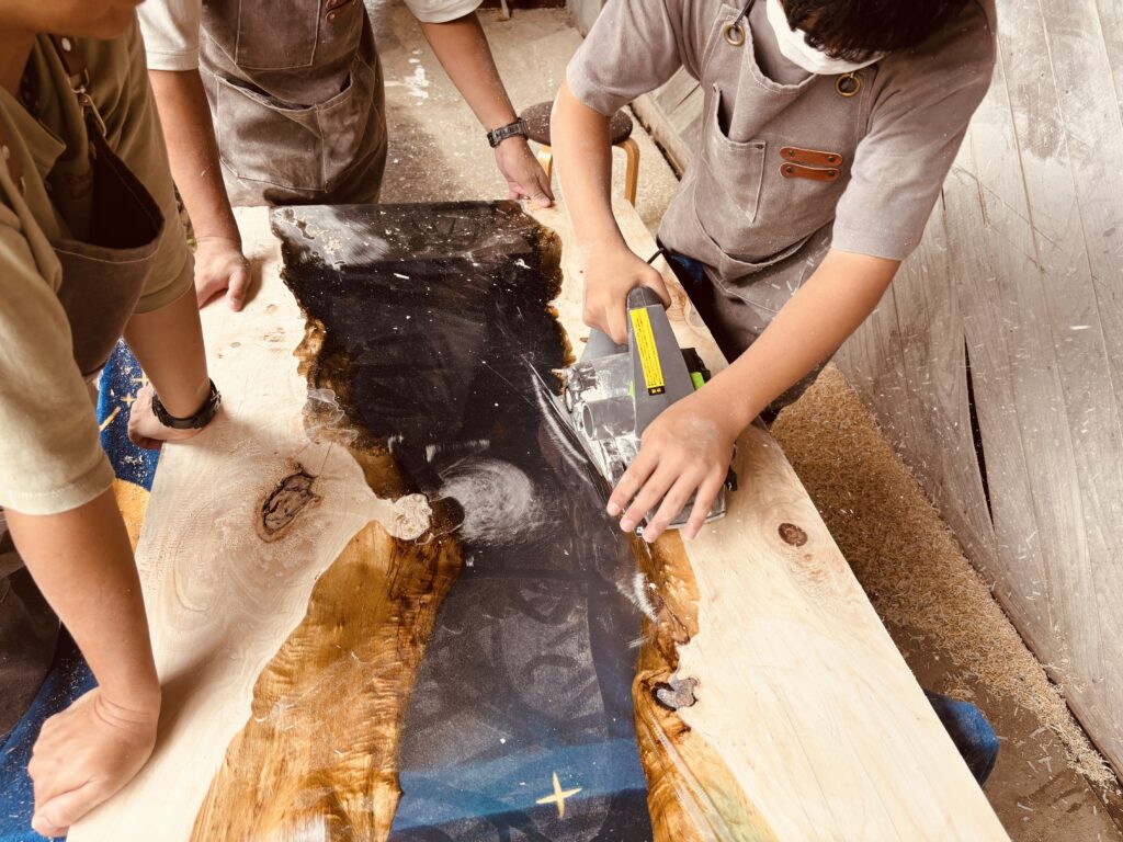 レジンテーブル製作体験ワークショップで参加者が電動工具を使い、木とレジンの境目を研磨している様子