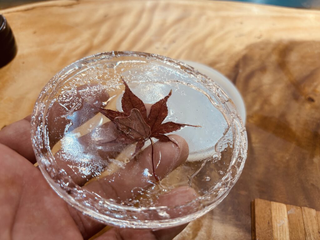 紅葉の葉を封入したUVレジンコースターの試作品を手に持ち、周囲に硬化不良の跡が見える様子。