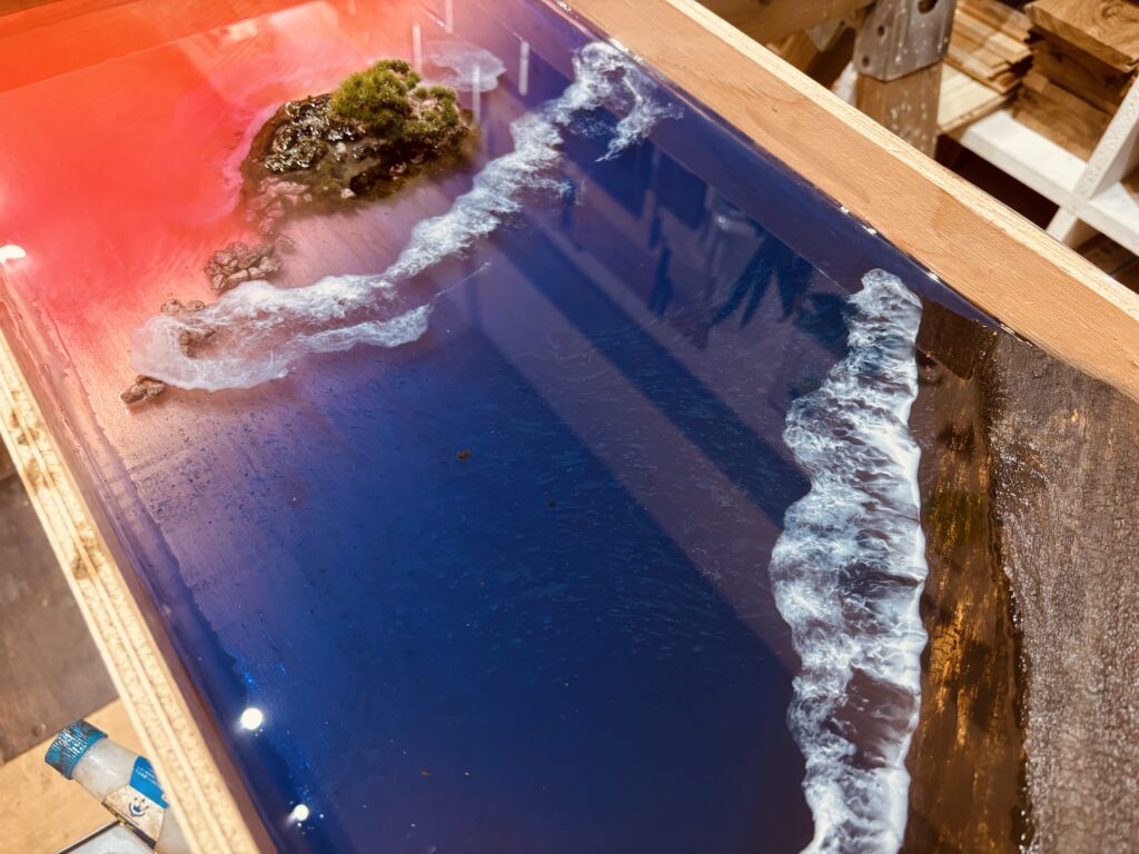 夕焼けに染まる空をイメージした赤と青のグラデーションレジンの海に、白い波が浮かび上がる制作途中のレジンテーブル
