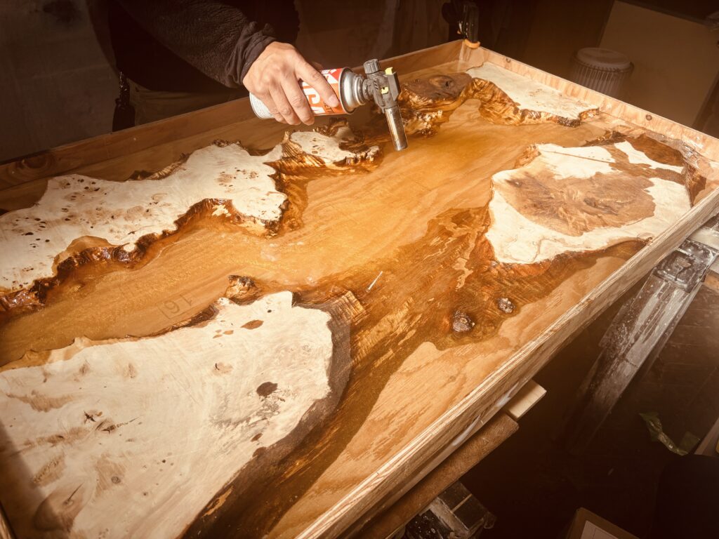 レジン表面の気泡をバーナーで除去している作業。ポプラ材とゴールドパールレジンの制作途中。