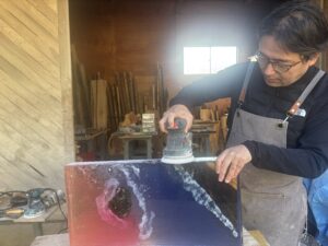 雨晴海岸の夕陽を表現したレジンテーブルを、制作体験の受講者が工房で研磨している全体風景