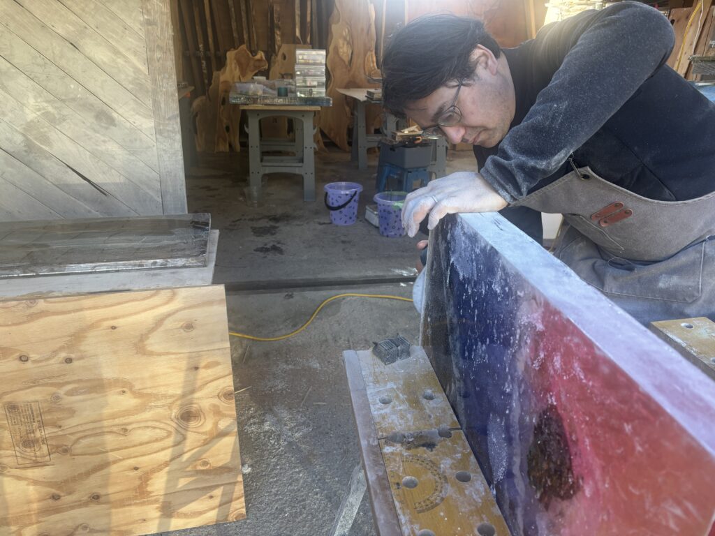 レジンテーブル制作体験の受講者が、雨晴海岸をモチーフにしたレジン天板の側面と厚みを確認しながら研磨している様子