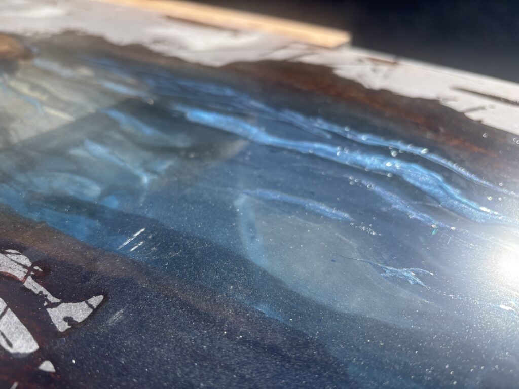 レジンテーブルの表面をクローズアップした写真。ブルーからクリアへ移ろう層と、光を受けて揺らぐレジンの質感が見える。