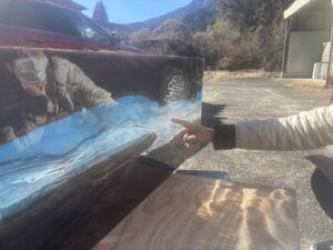 完成途中のレジンテーブルを横から見た様子。ブルーからクリアへと流れる層を指差しながら確認している場面。アフリカンブラックウッドの荒々しい木目が見える。