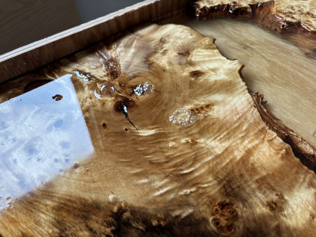 ゴールド顔料を散りばめたレジンを流し込み、層を重ねて硬化させている途中のレジンテーブル。木の瘤や杢目の間に、金色の流れが静かに広がっている。