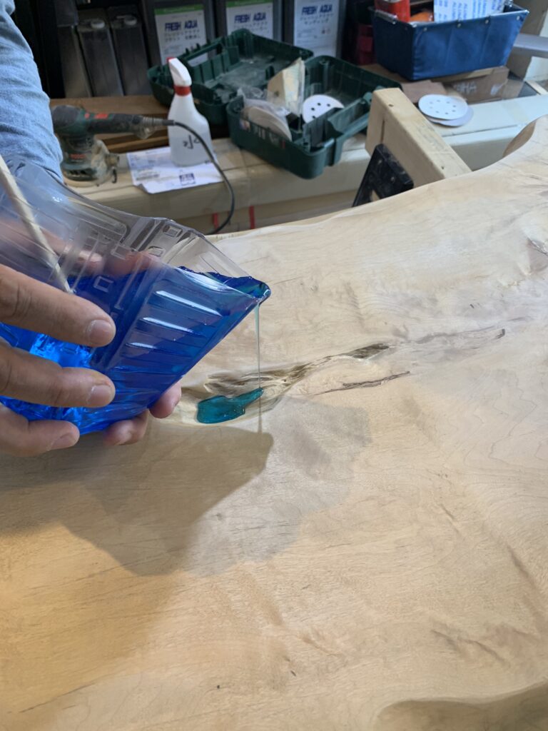 トチノキの割れ部分にブルーのレジンを少量ずつ流し込んでいる工程写真。