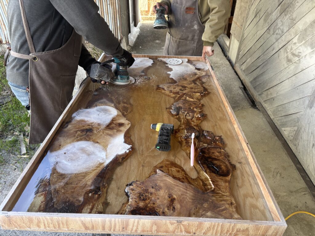 固まったレジン表面をサンダーで研磨し、内部に残った気泡跡を削り出しているレジンテーブル制作体験の作業風景。