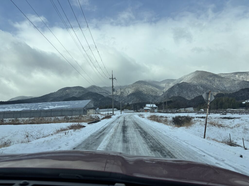 大雪で白く覆われた山麓の道路を、車内から撮影したアトリエへ向かう道中の風景。