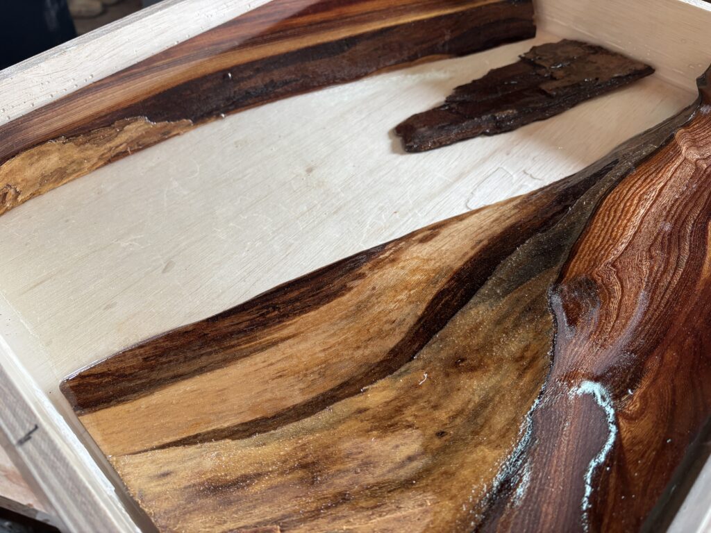 木枠の中で、ケヤキの木材に沿うように透明レジンの層を作り、表面が濡れたように光っているクローズアップ。